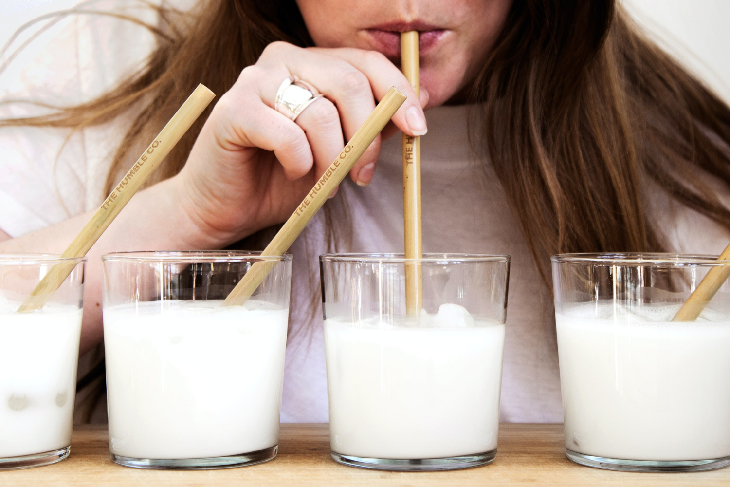 Four glasses of milk in a row, women sipping out of third glass with a straw; what you need to know about IBS and lactose intolerance